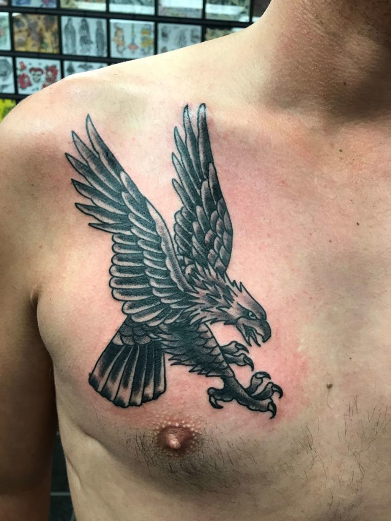 Chest tattoo of a black and grey eagle with spread wings and detailed feather work