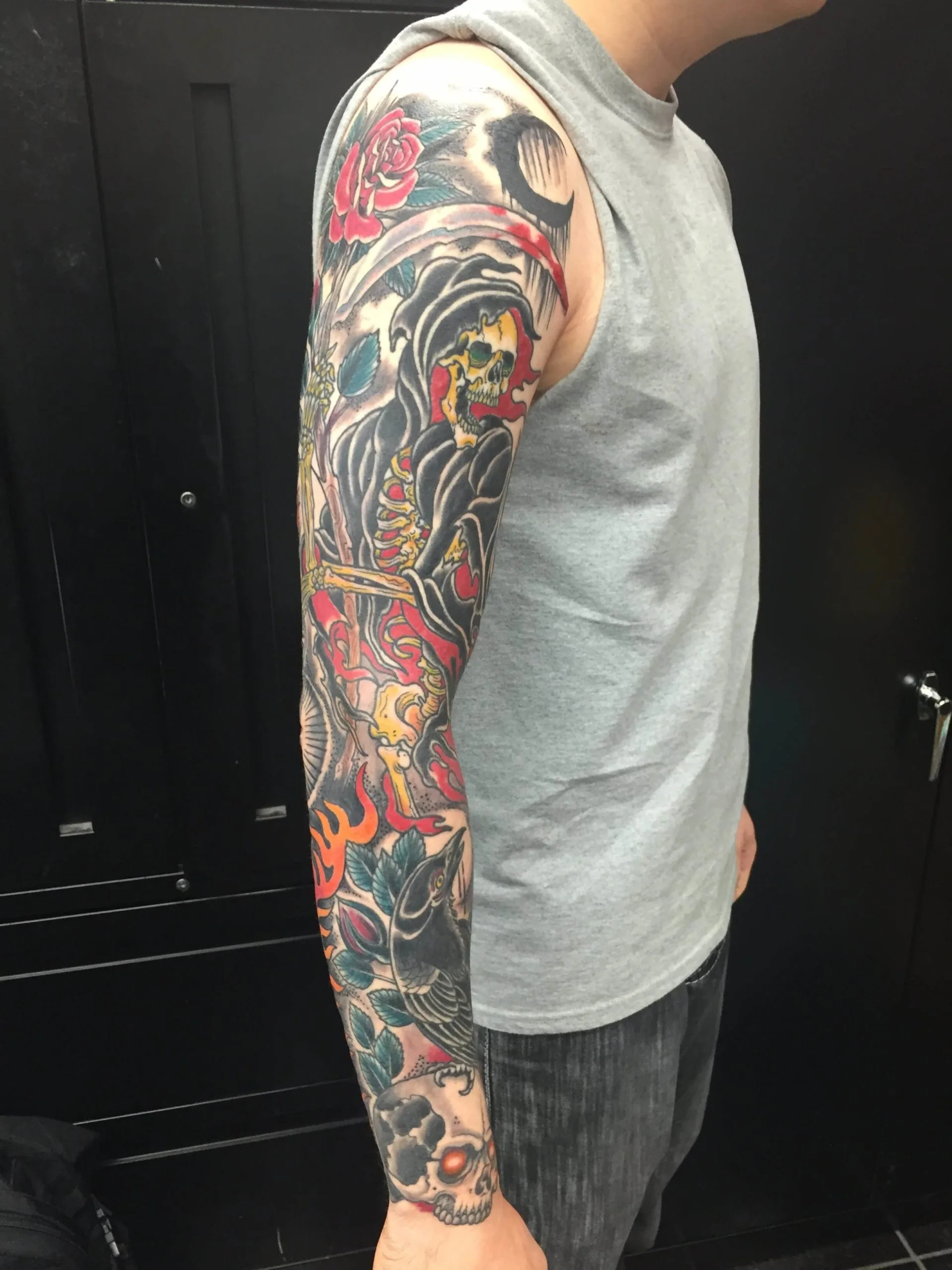 Full arm sleeve with a Grim Reaper holding a scythe, a red rose, flames, and a skull near the wrist