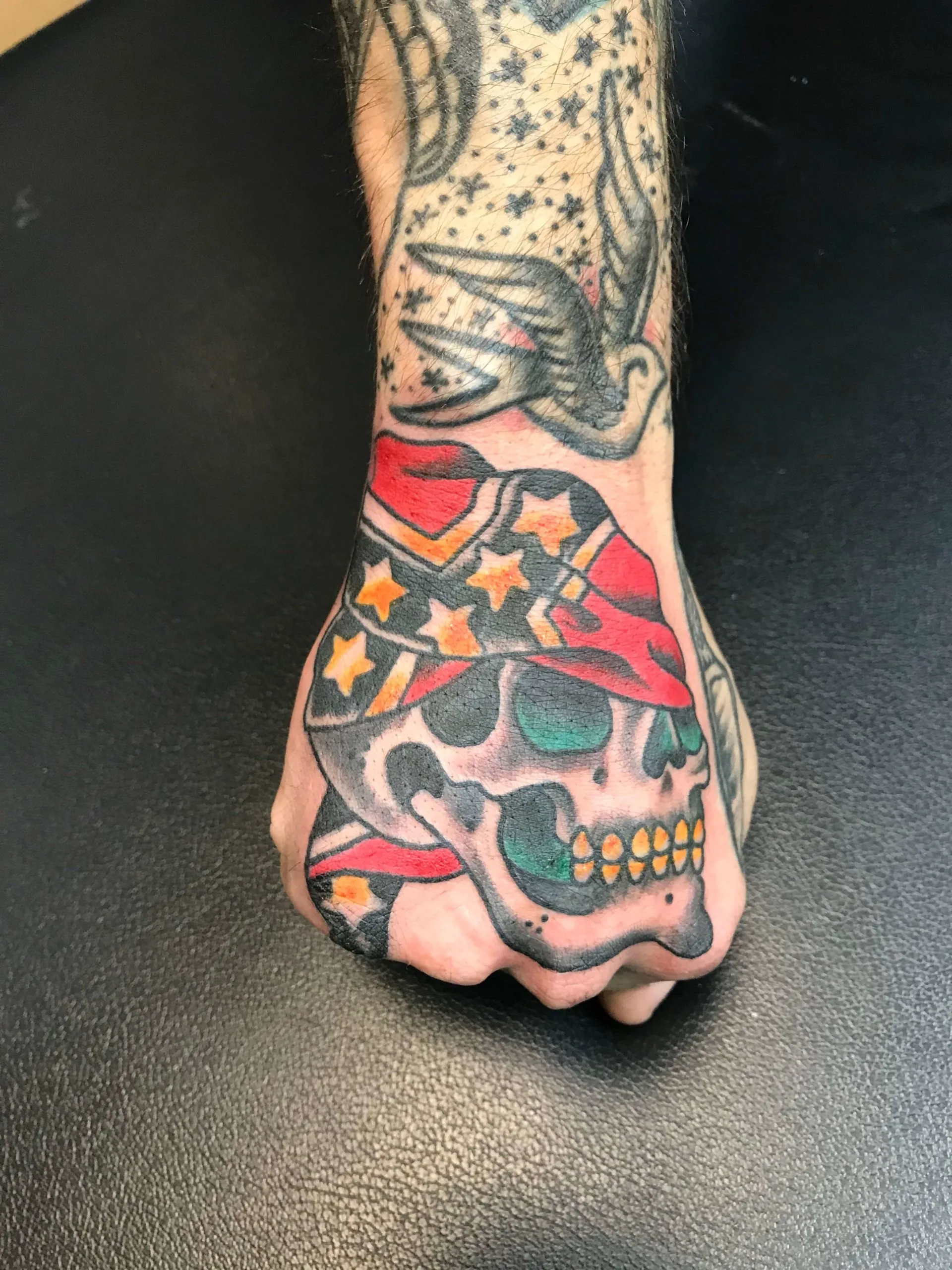 Skull wearing a red bandana with stars on the hand, with a swallow tattoo above on the wrist