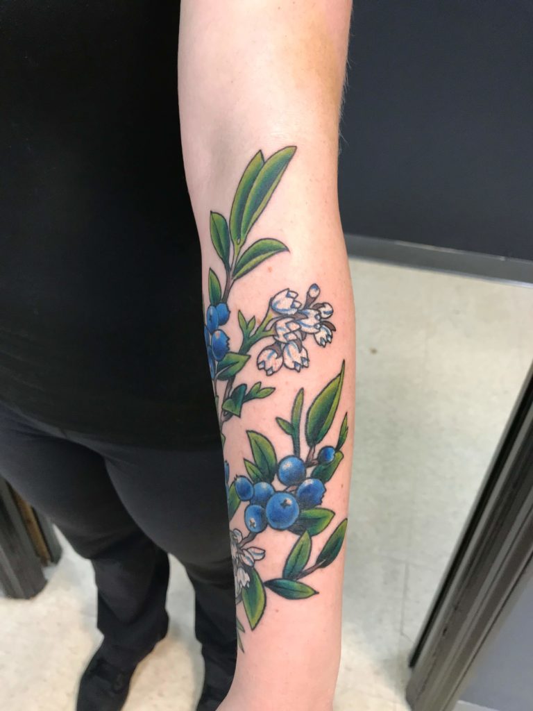 colour forearm with a botanical branch of blueberries, white blossoms, and green leaves