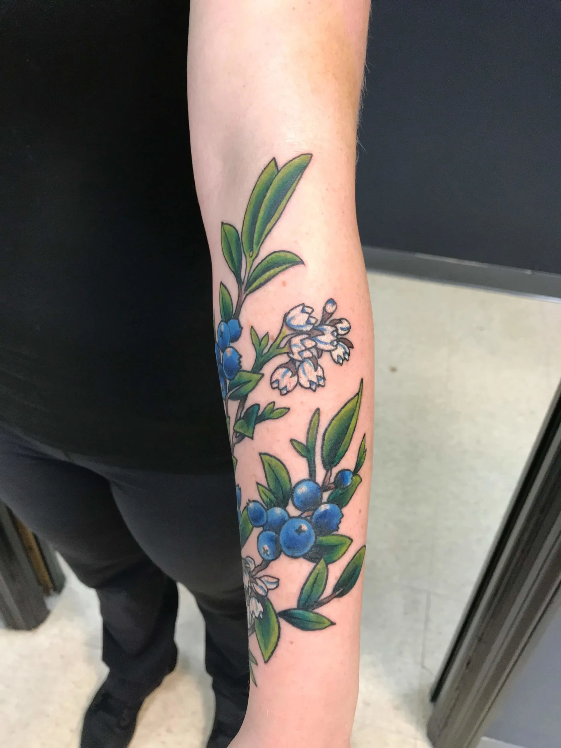 colour forearm with a botanical branch of blueberries, white blossoms, and green leaves