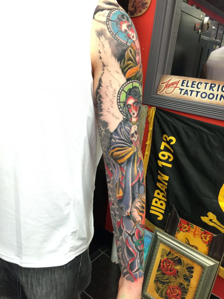 Colour sleeve of a haloed winged figure holding a skull, above a tiger's head