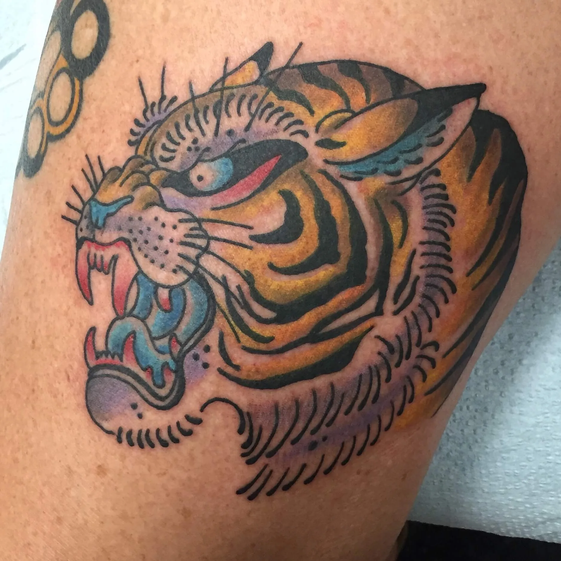 Colour close-up tattoo of a tiger head with orange stripes and teal shading