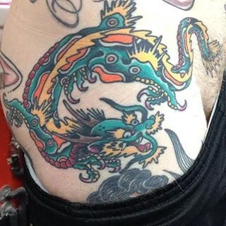 Small color tattoo above the waistband of a teal dragon-like creature with red and gold accents