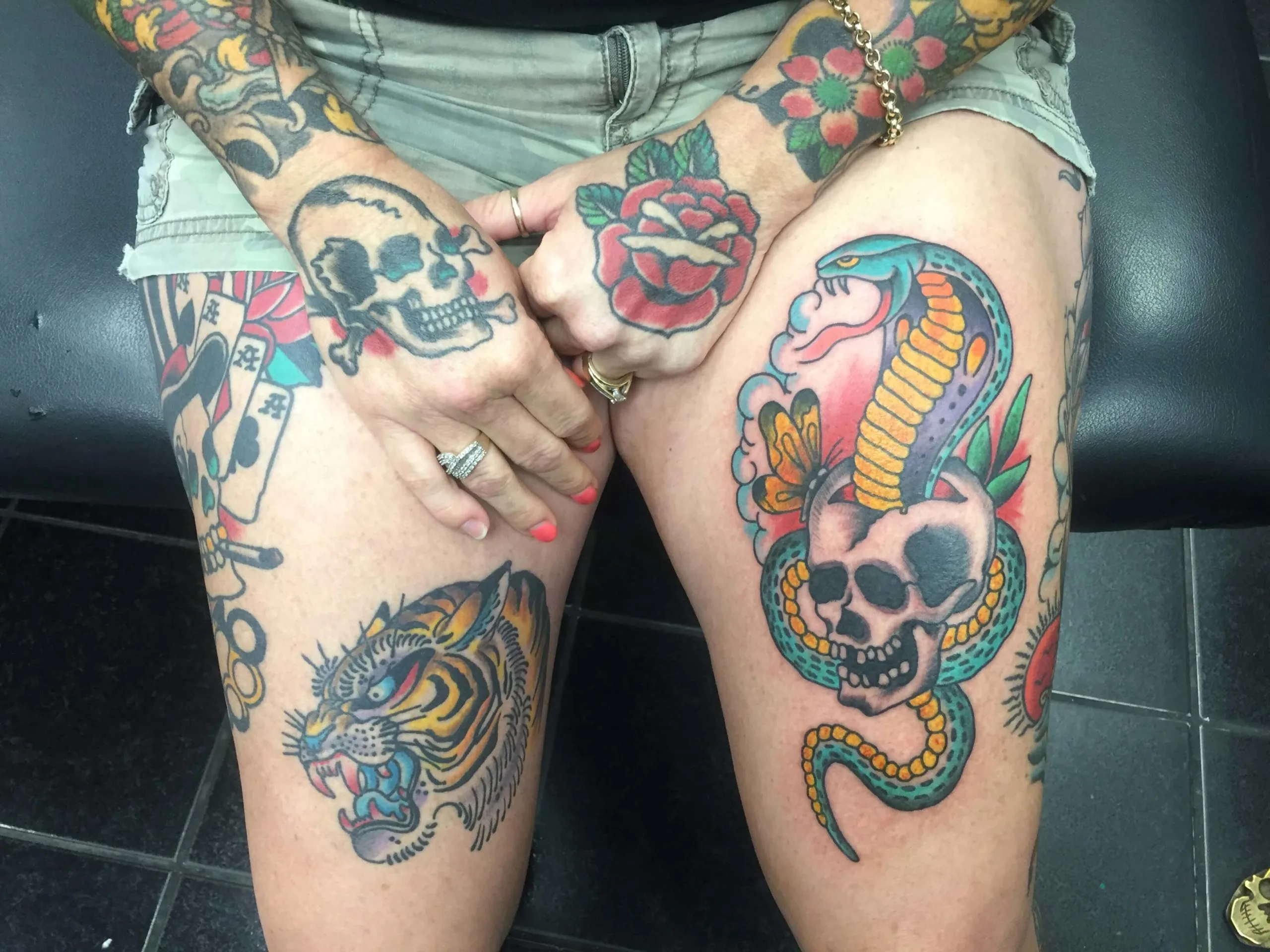 Colour thigh tattoos of a skull with roses and a cobra wrapped around a skull, with a rose near the wrist