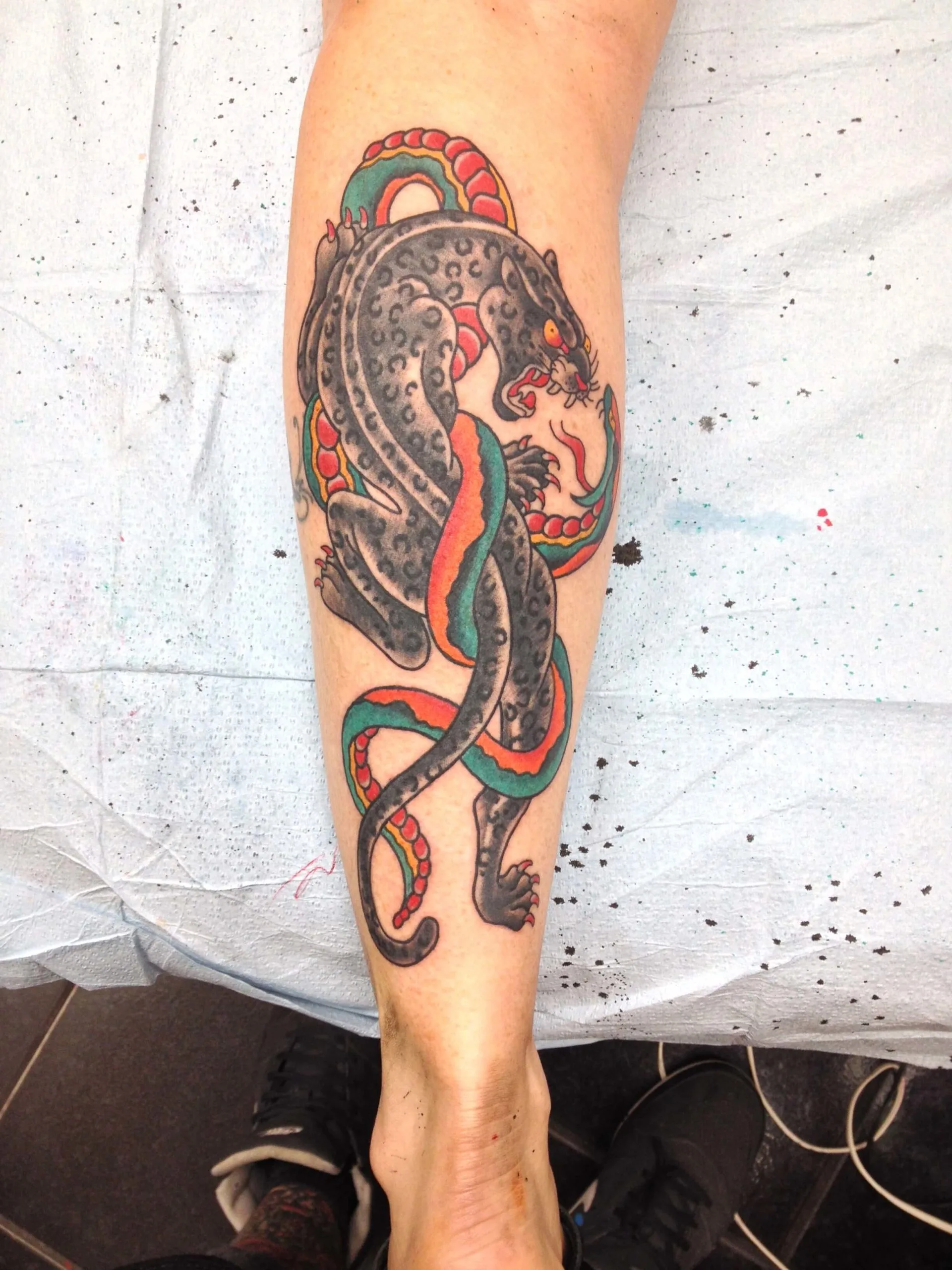 Black spotted panther entwined with an orange-and-teal snake on the lower leg