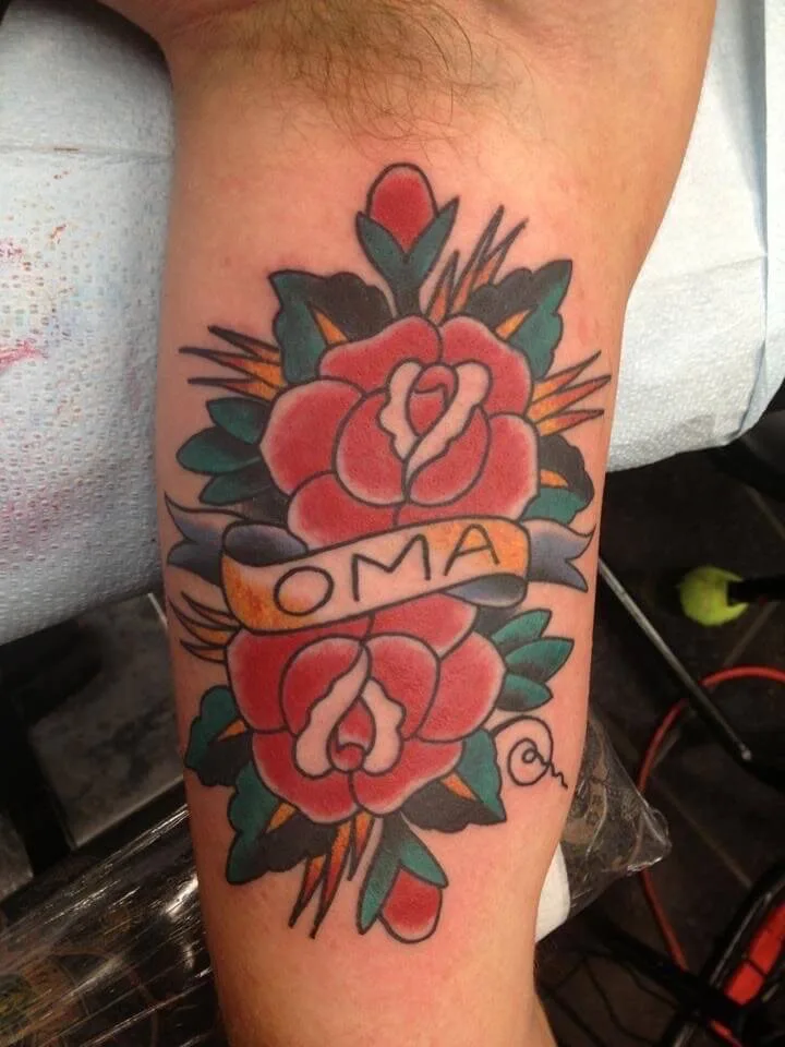 Forearm with two red roses, green leaves, and a banner reading 'OMA' in colour