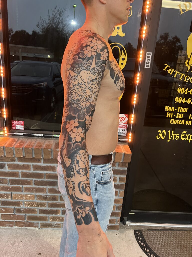 Black and grey full arm sleeve with a foo dog's face among cherry blossoms