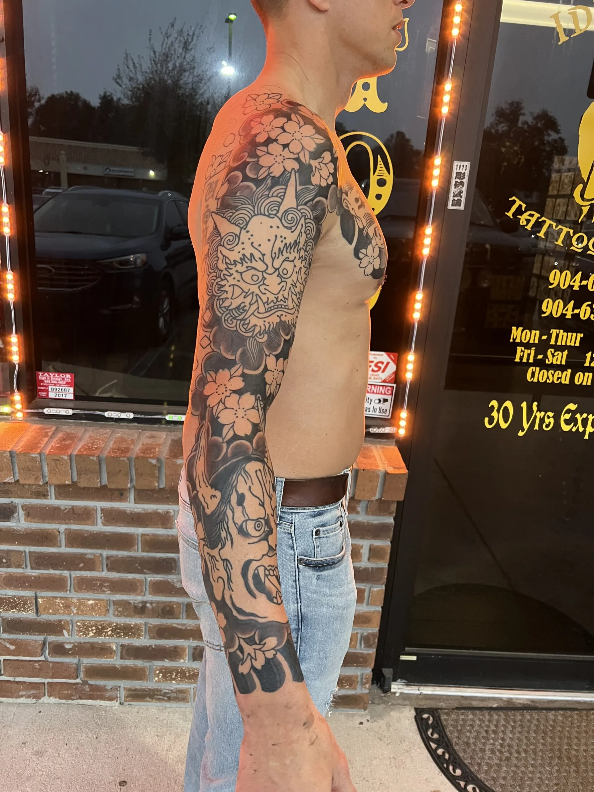 Black and grey full arm sleeve with a foo dog's face among cherry blossoms