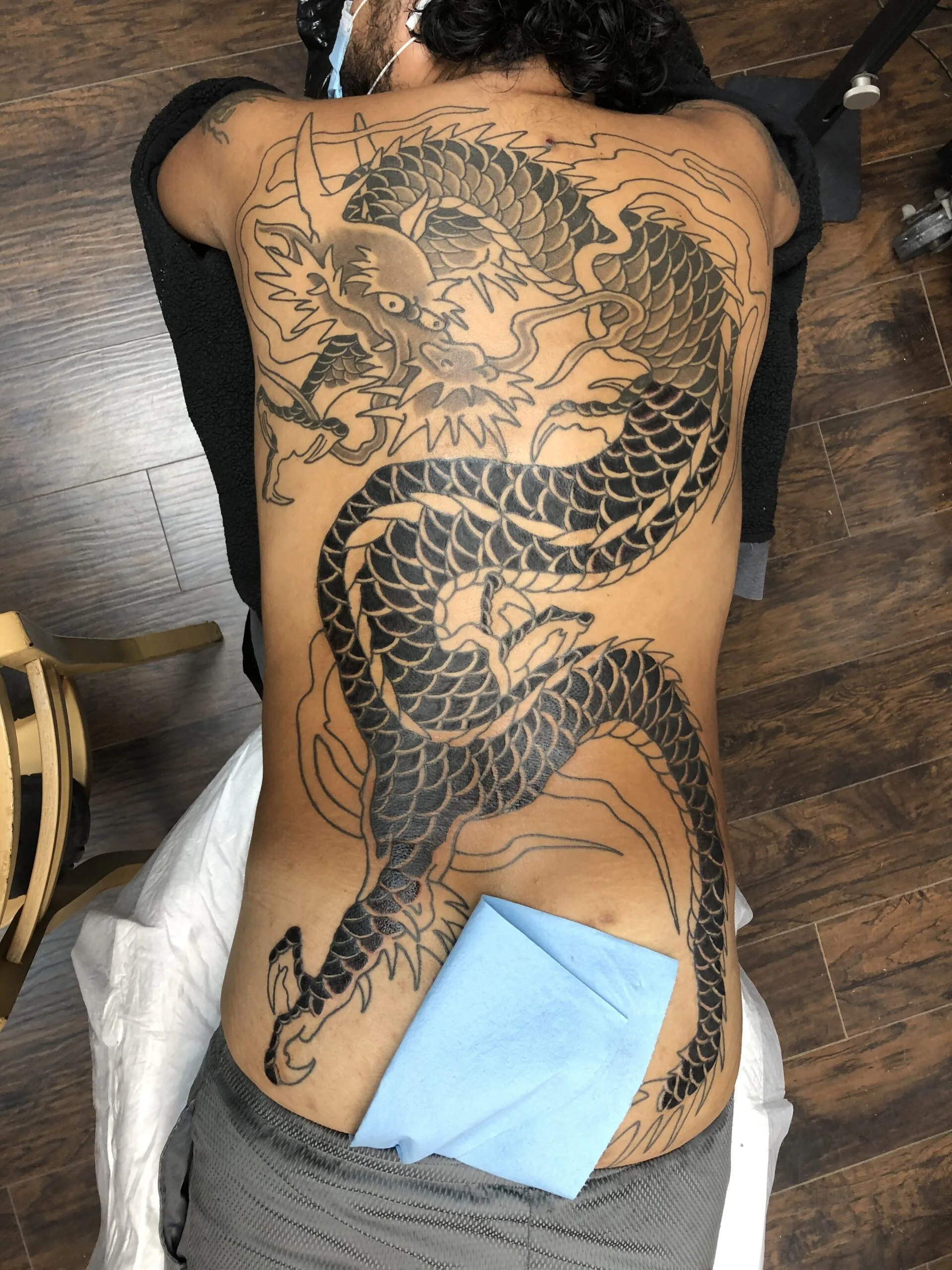 Japanese dragon outline in progress across the back, unshaded linework, person lying face-down