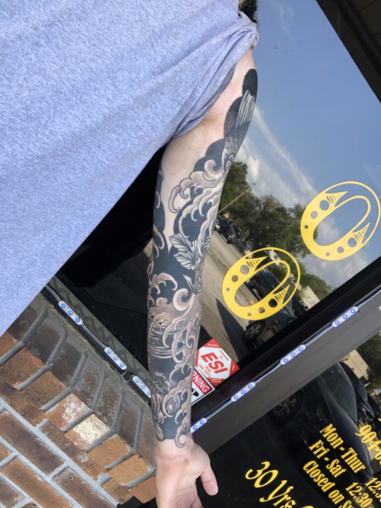 black and grey full sleeve with layered cloud and wave patterns and a floral accent on the forearm