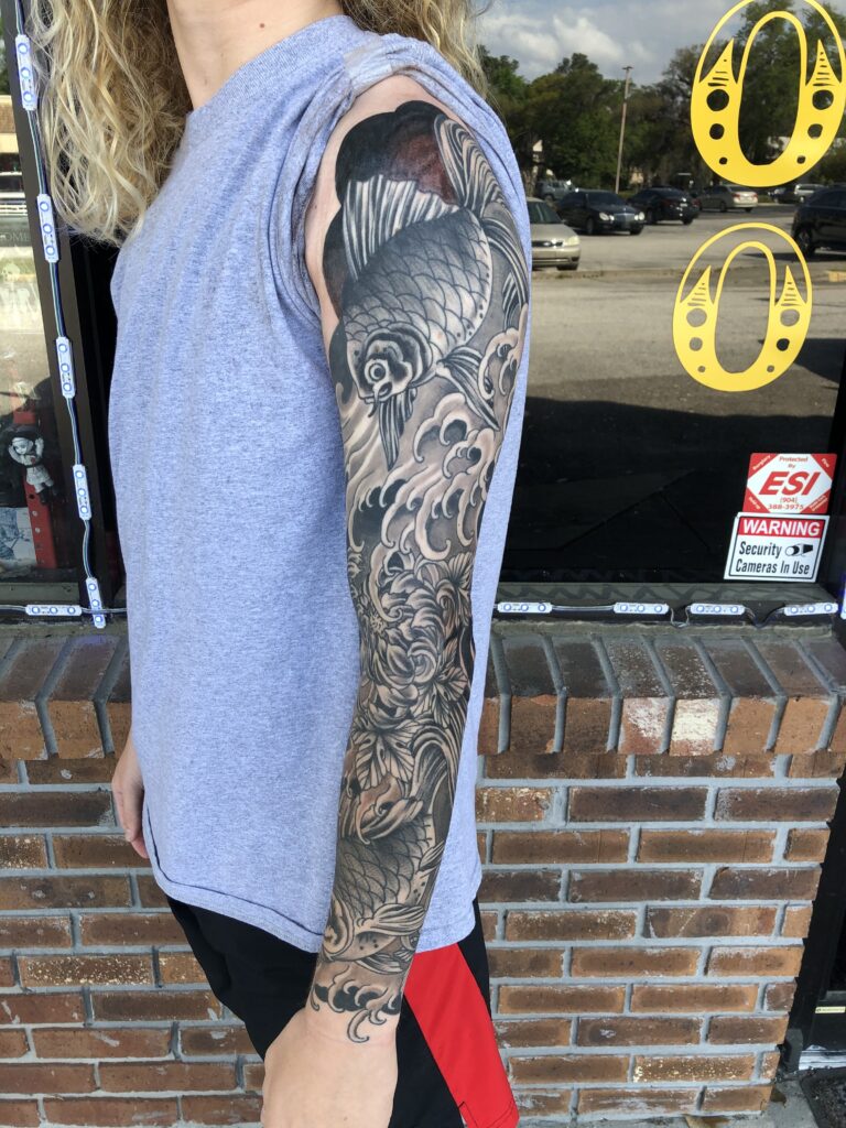Full arm sleeve in black and grey with a swimming koi fish and rolling wave patterns