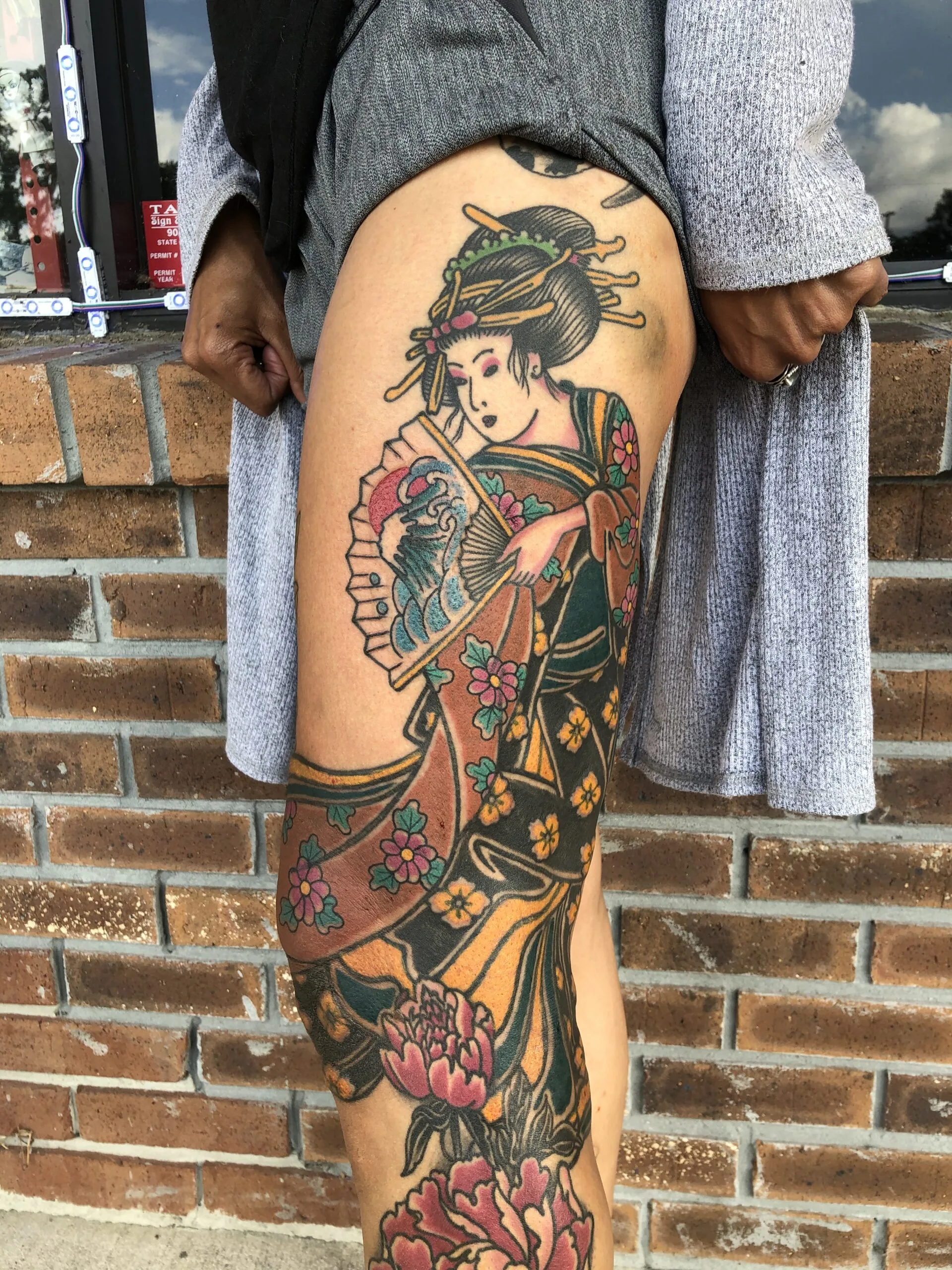 Figure in a kimono holding a fan on the thigh, with pink peonies and gold ornamental patterning below