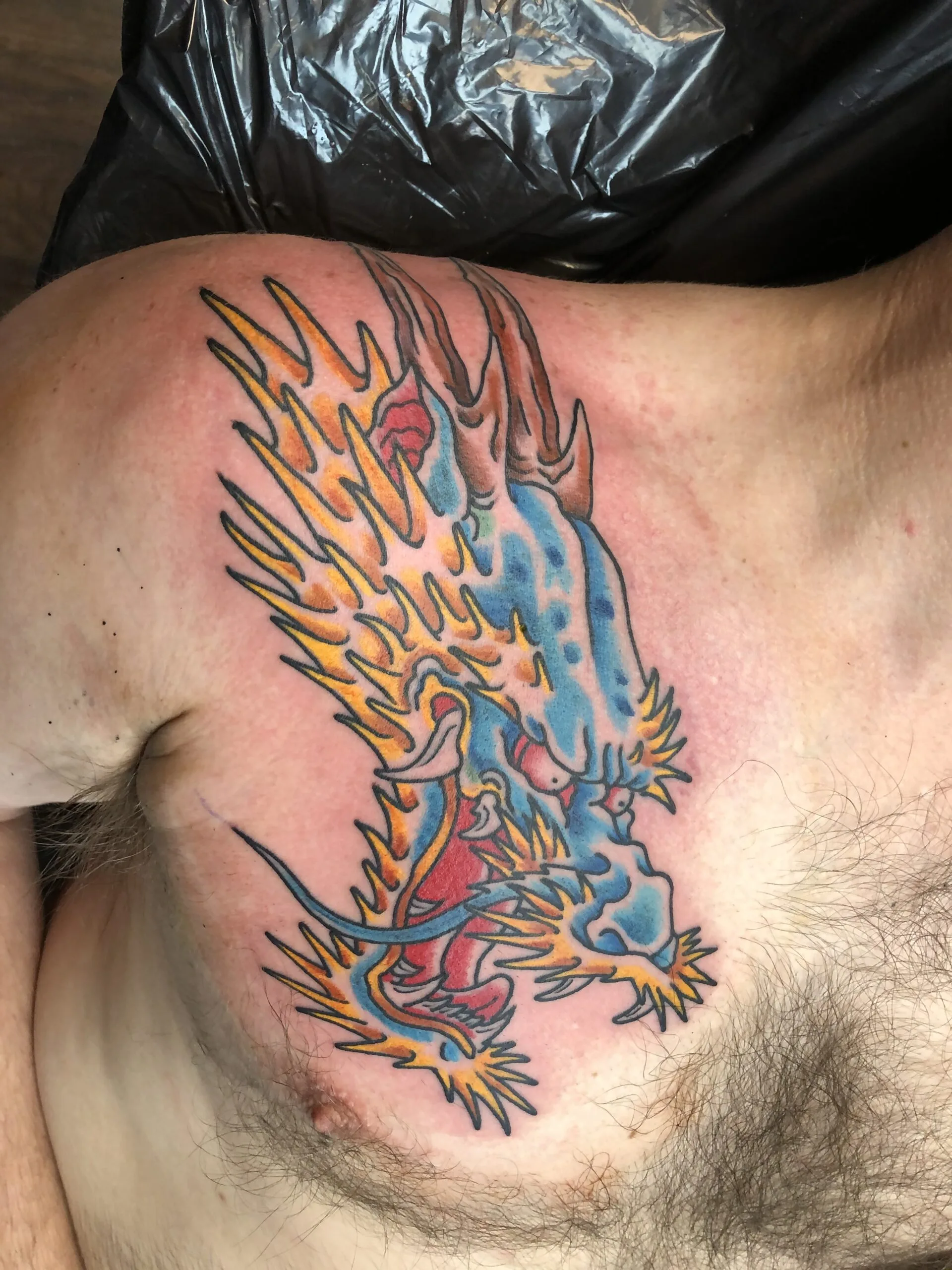 Colour chest tattoo of a blue dragon with orange flame-like spikes