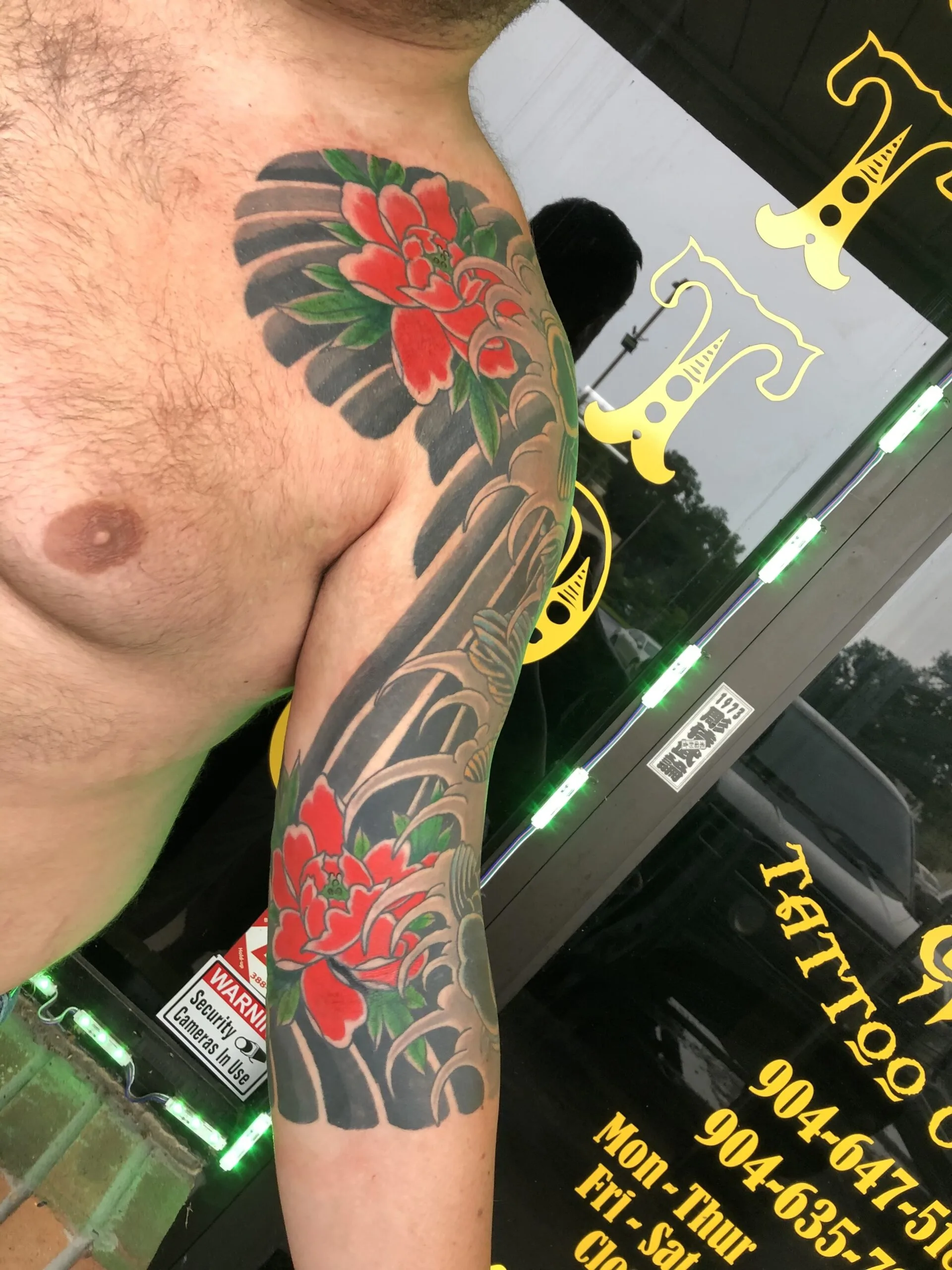 Red peonies on the shoulder above black-shaded banding down the upper arm