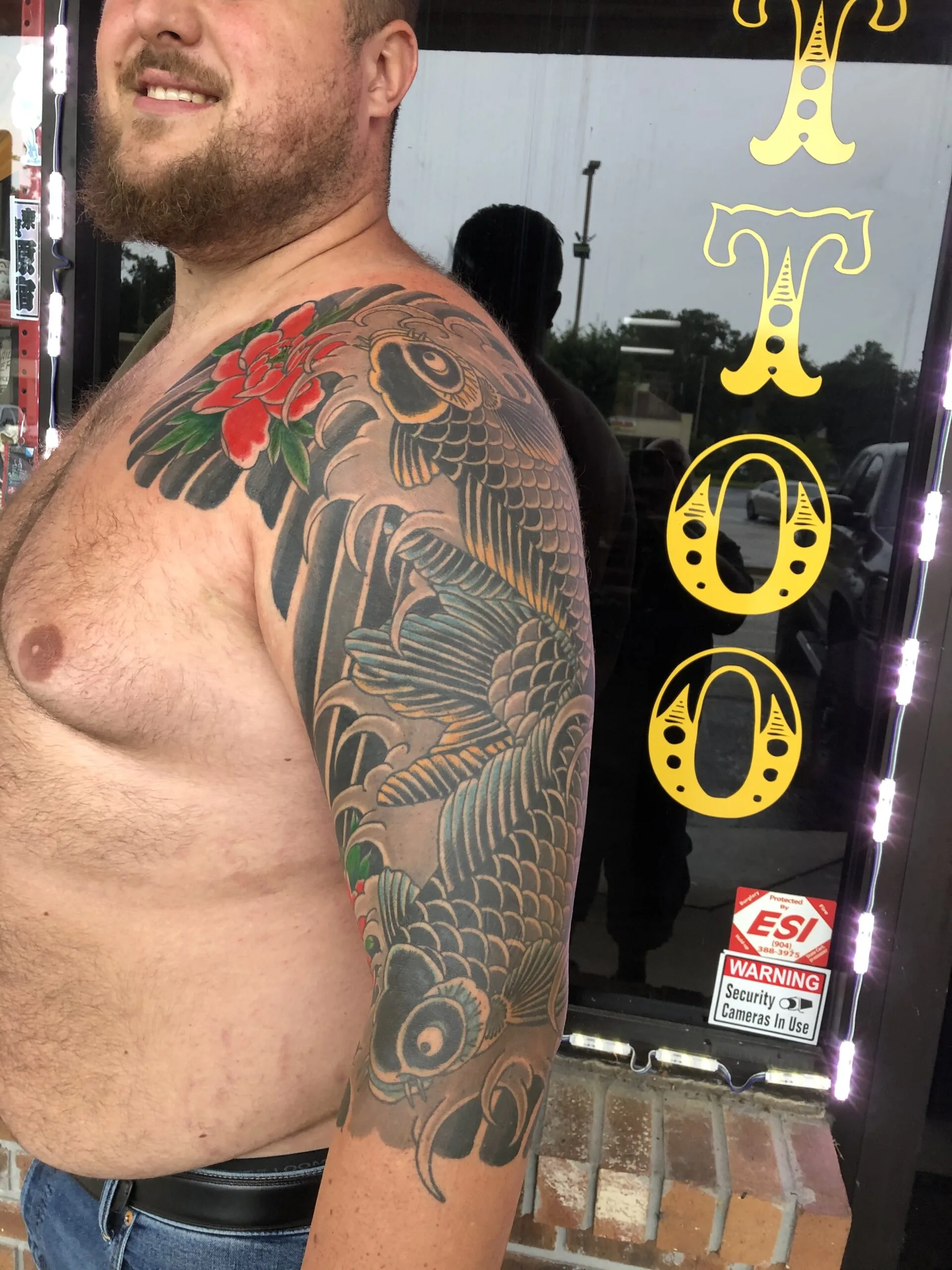 Shoulder and upper arm with a large grey and black koi fish and red flowers, black and grey with colour accents