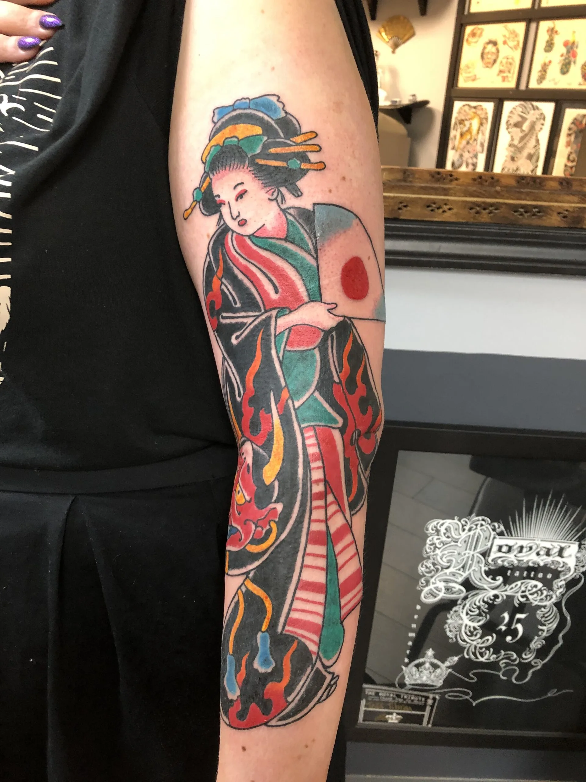 Color upper arm tattoo of a Japanese woman in a red and green kimono holding a fan, part of a full sleeve