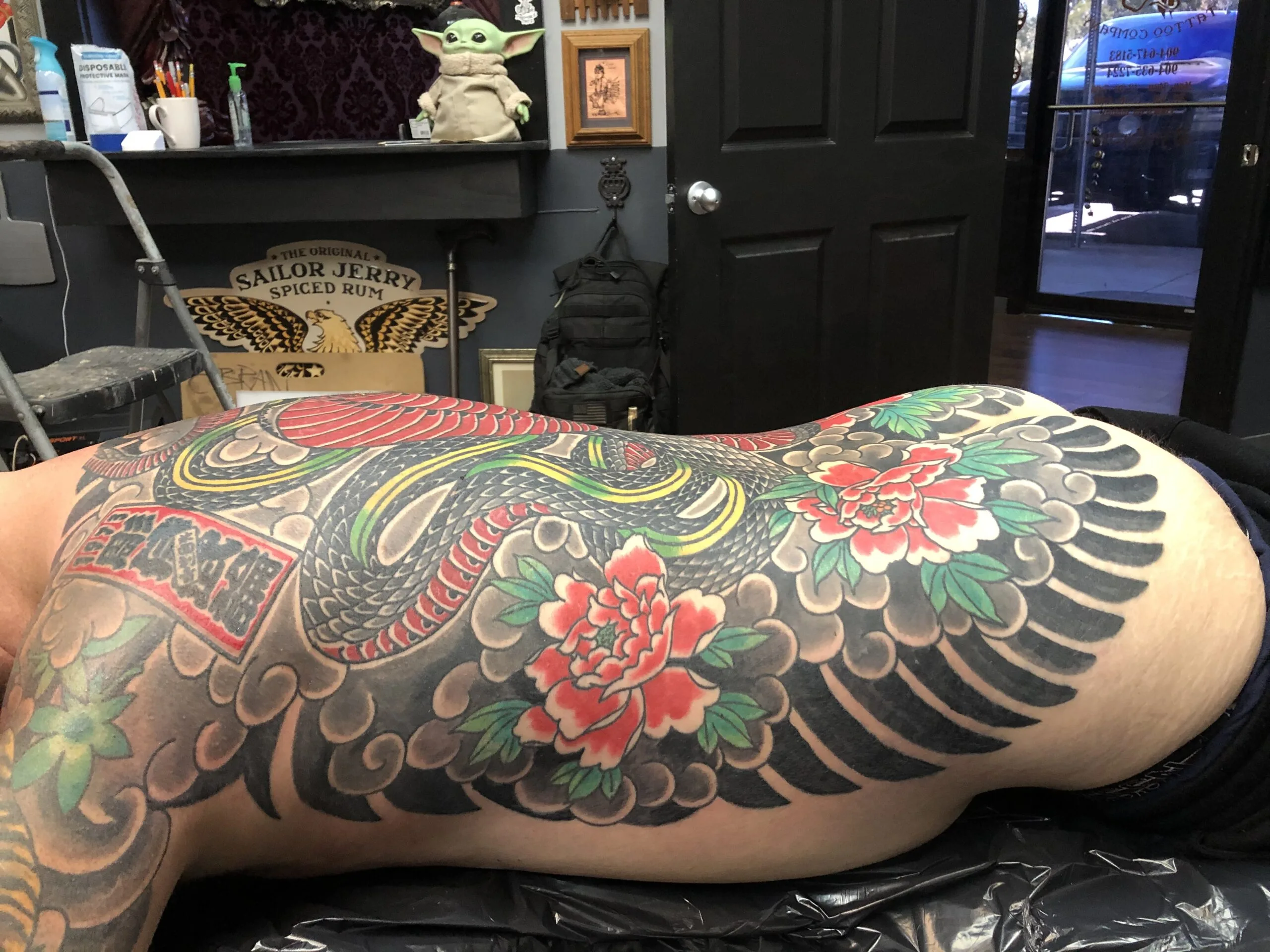 Black, red, and green tattoo of a coiled snake with peonies across the back and side torso