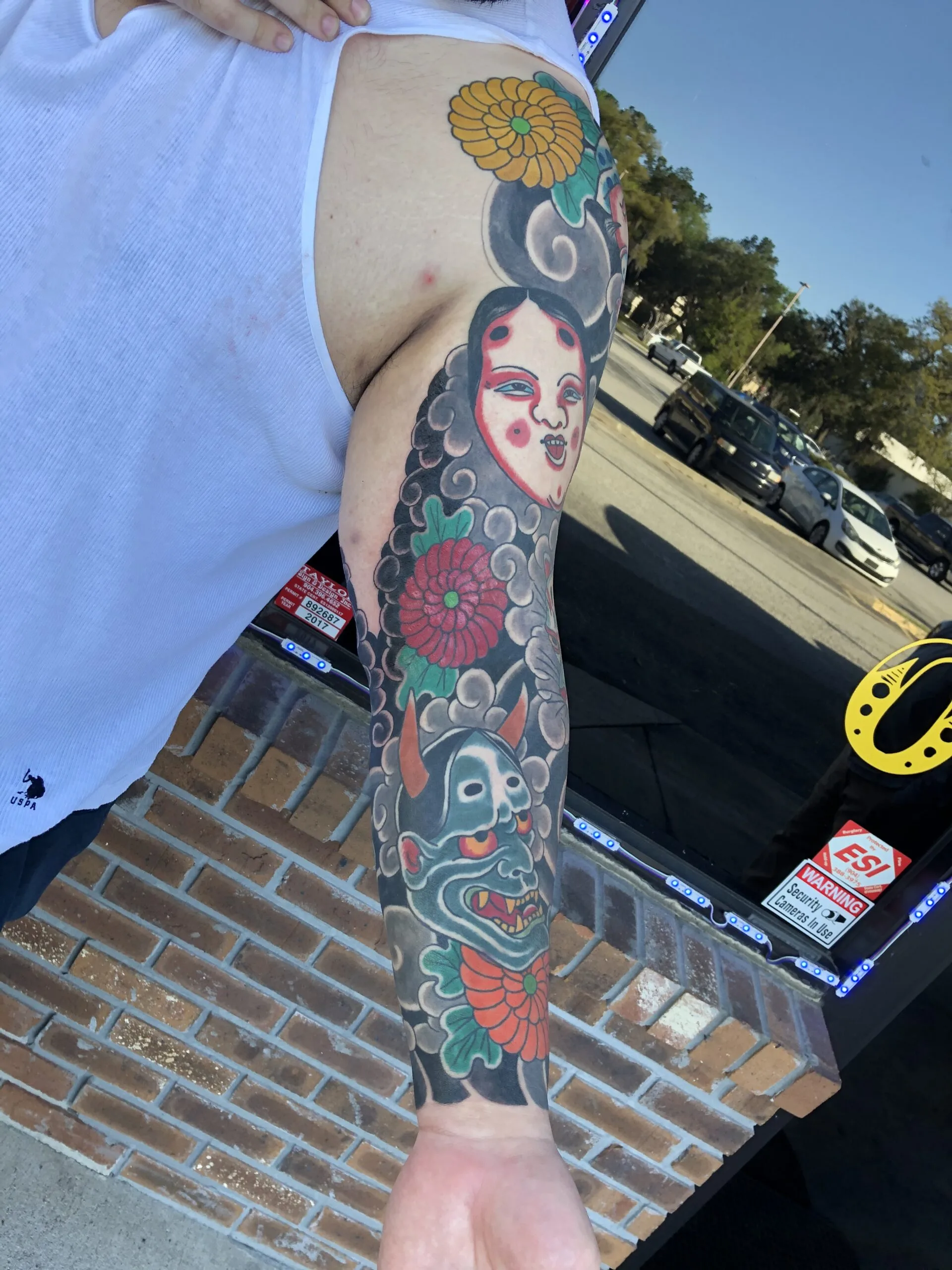 Full arm sleeve with a chrysanthemum, a pale face amid clouds, and a green horned mask with red flowers