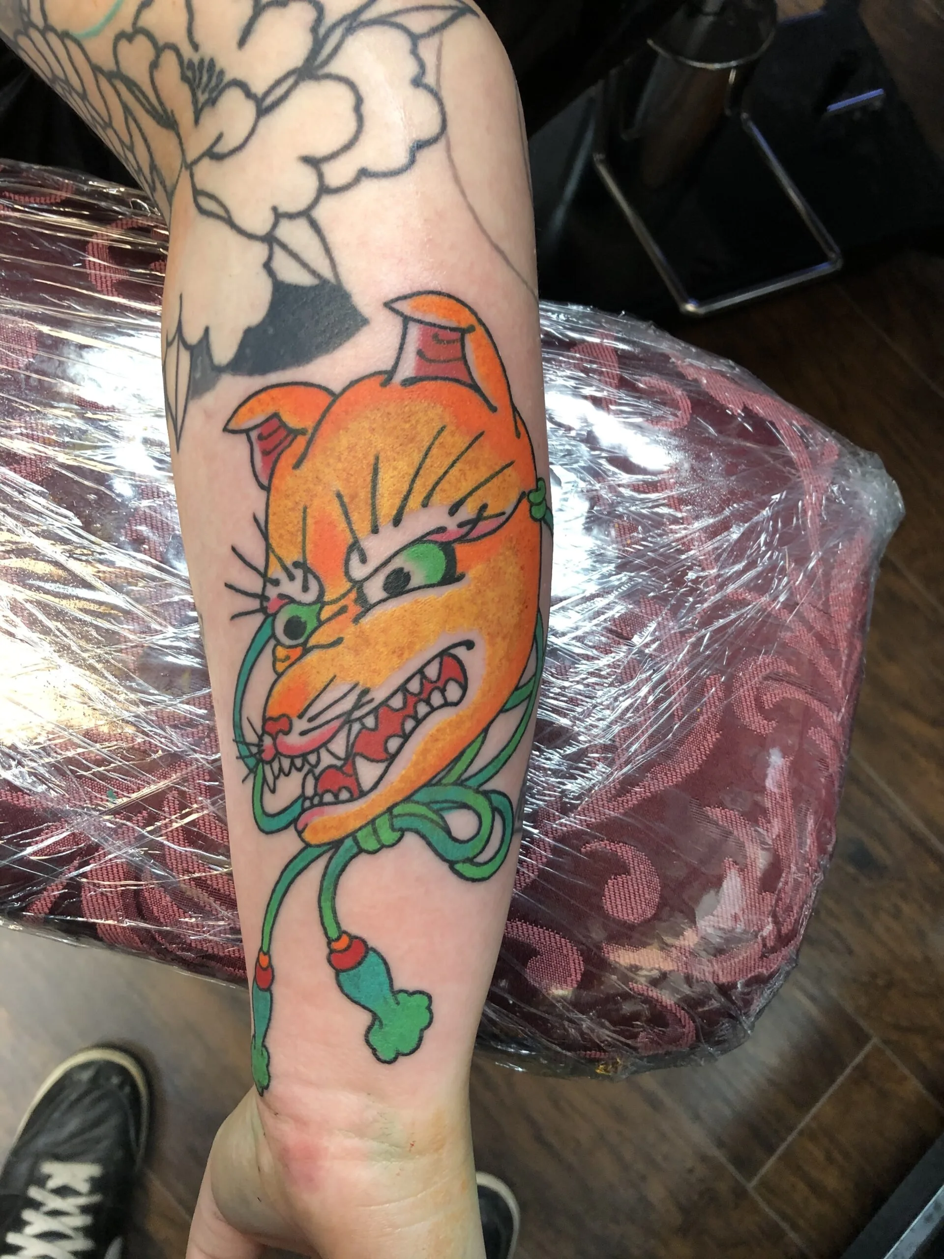 Orange fox-mask tattoo on the forearm with a green cord tied beneath it