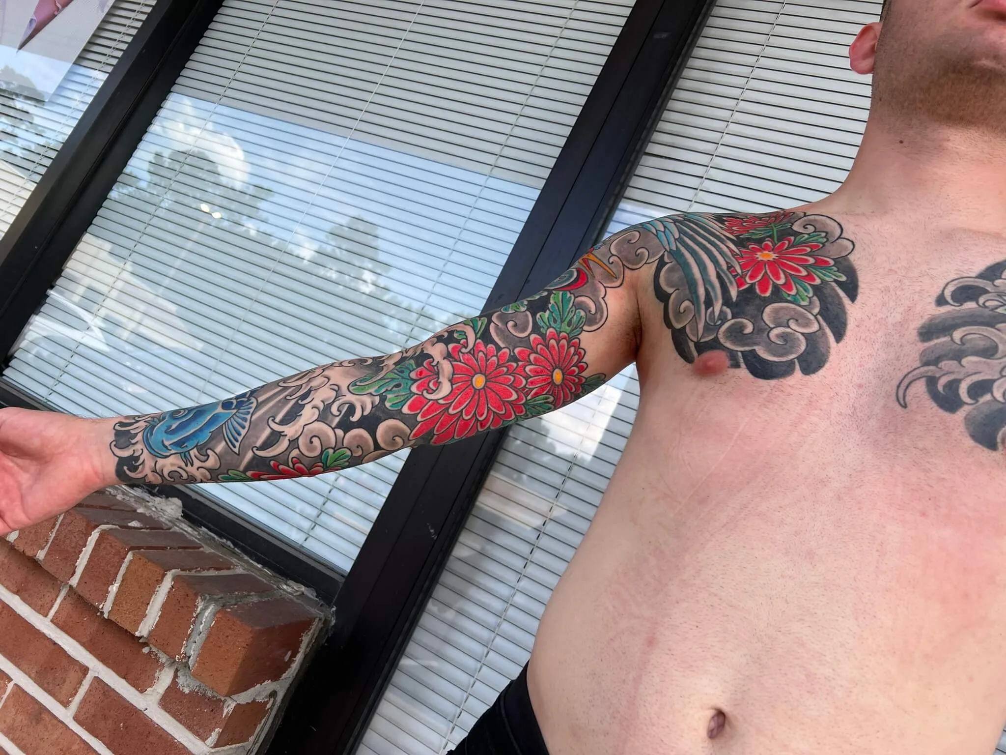 colour arm extended forward showing a full sleeve of red and green chrysanthemums, grey wave clouds, and a small blue koi