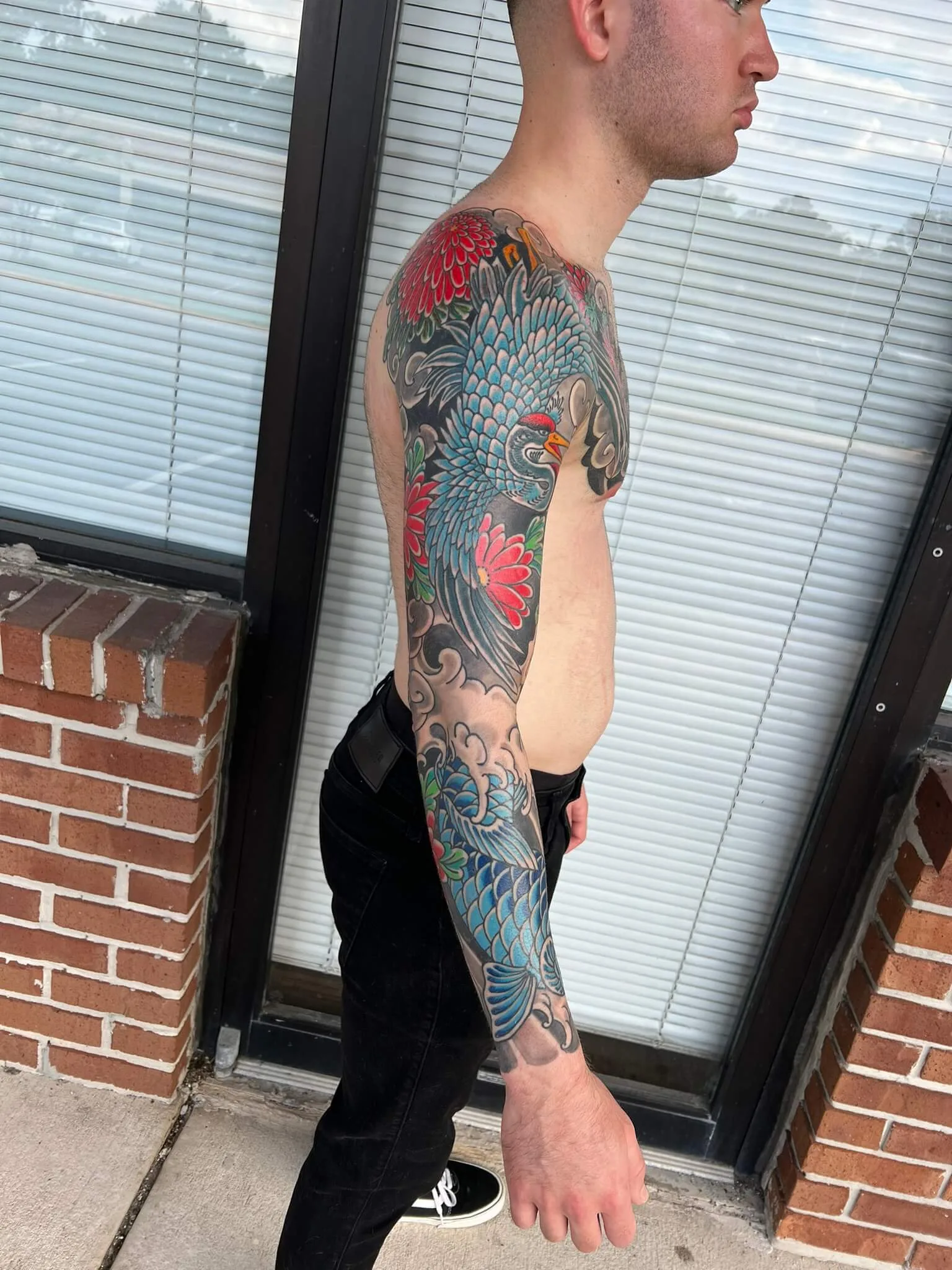 Color full-arm sleeve with a blue-grey crane and red chrysanthemums at the shoulder, transitioning to a blue koi lower on the arm