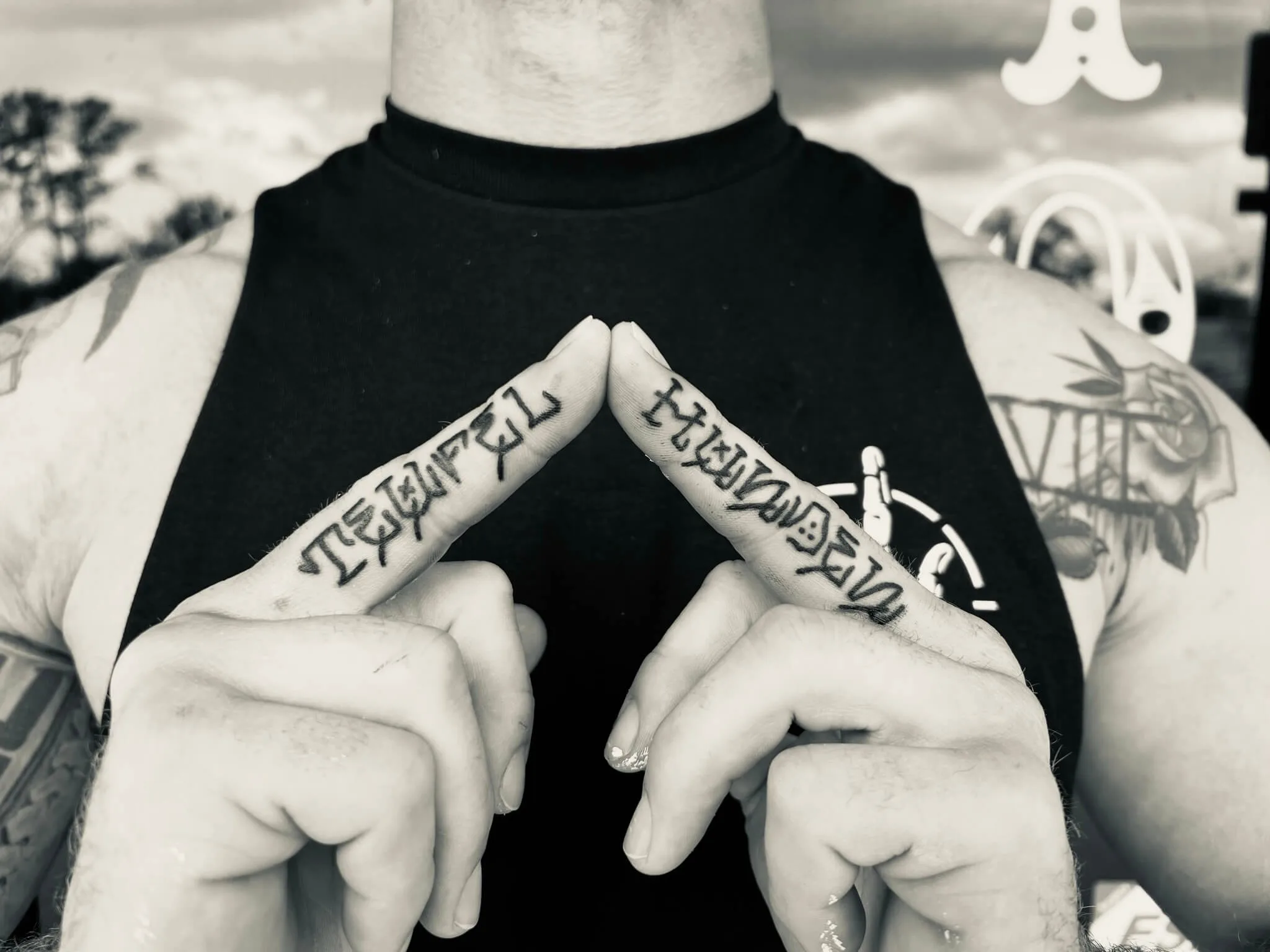 black and grey gothic-script lettering tattooed on two fingers, hands pressed together