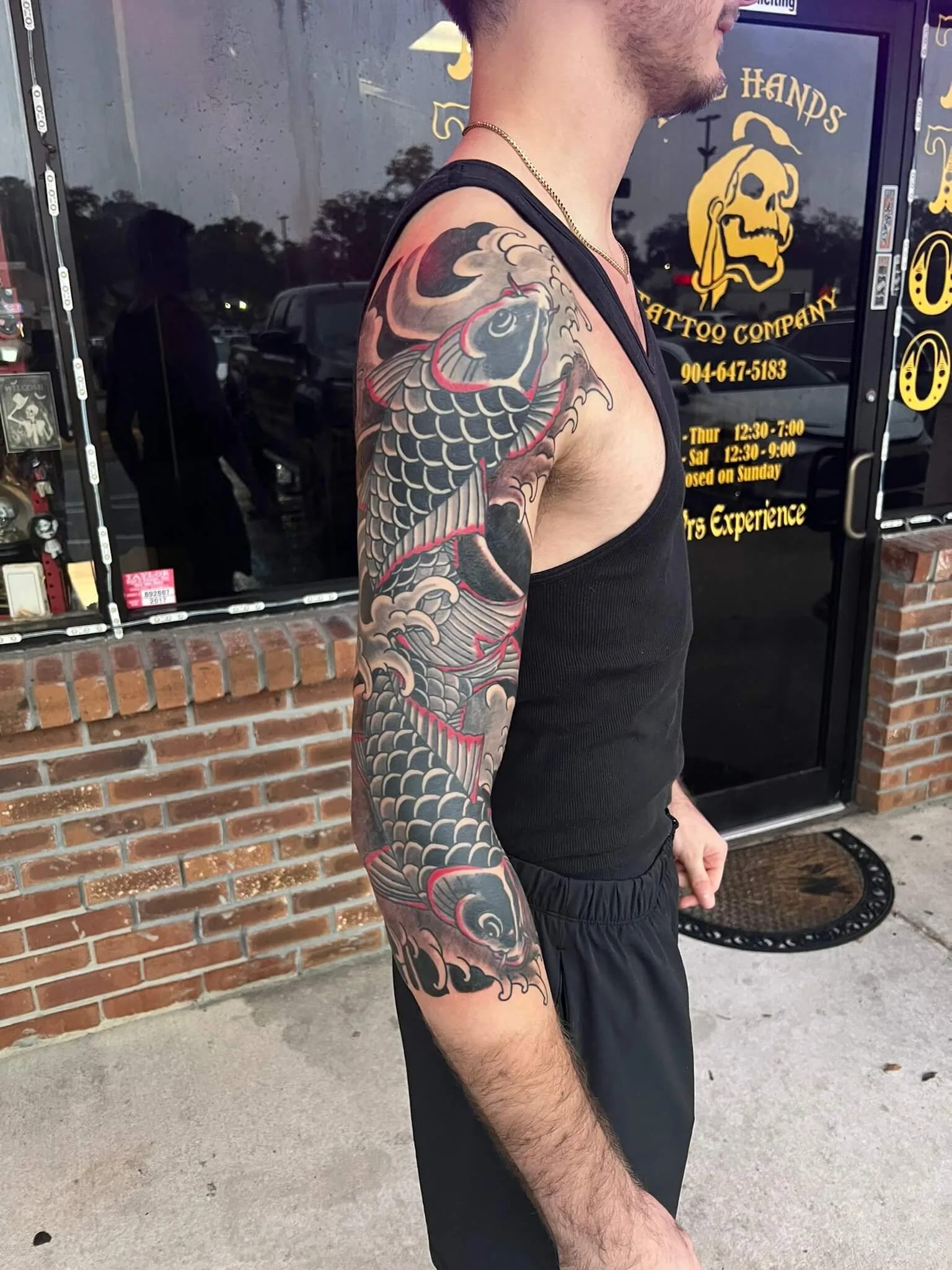 Color full-arm sleeve featuring a black and grey koi fish leaping through waves with red accents, shoulder to wrist