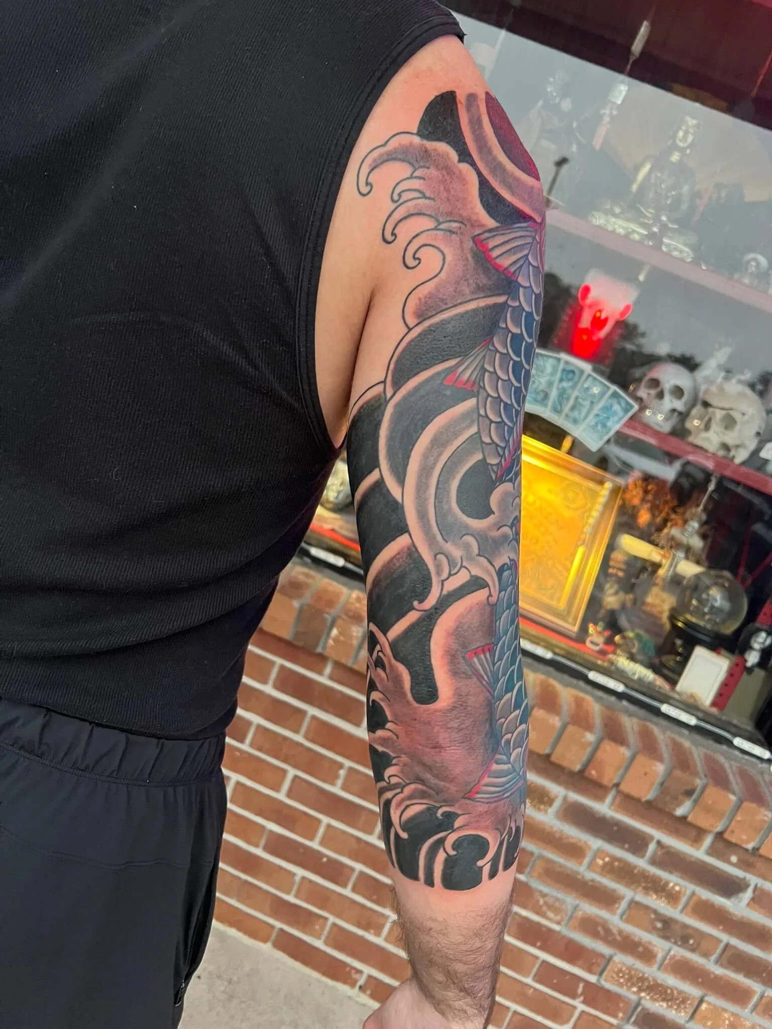 Full arm sleeve with a blue-grey koi fish, red fin details, and grey wave crests