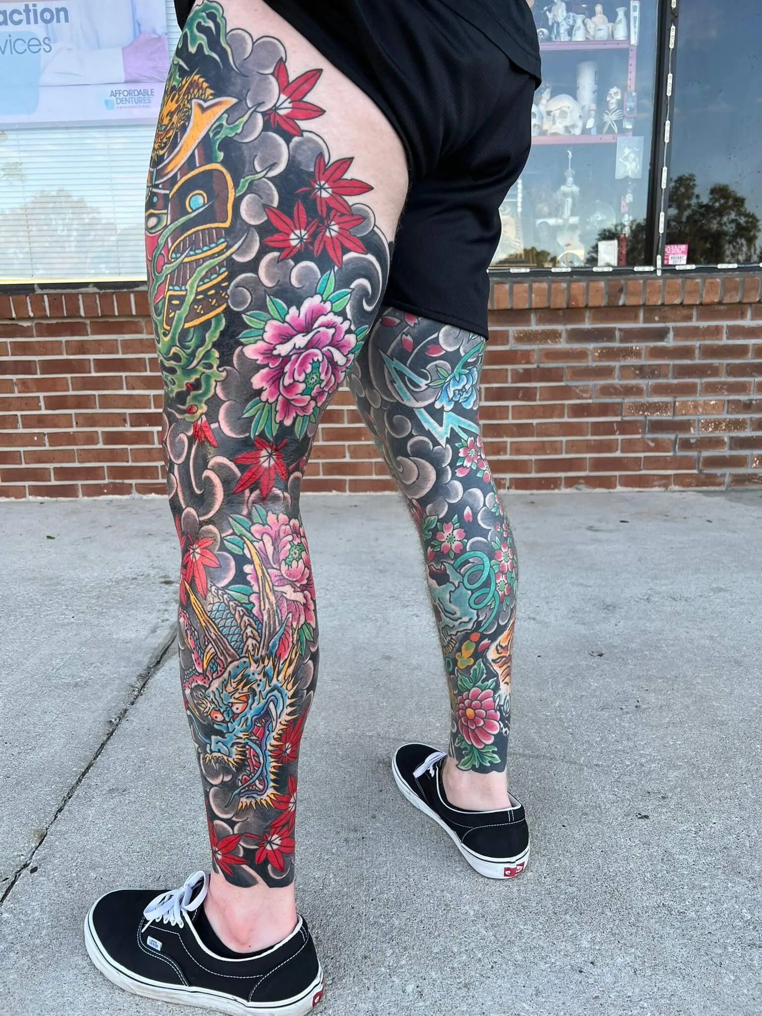 Full leg tattoos on both legs with dragons, red maple leaves, pink peonies, and grey clouds