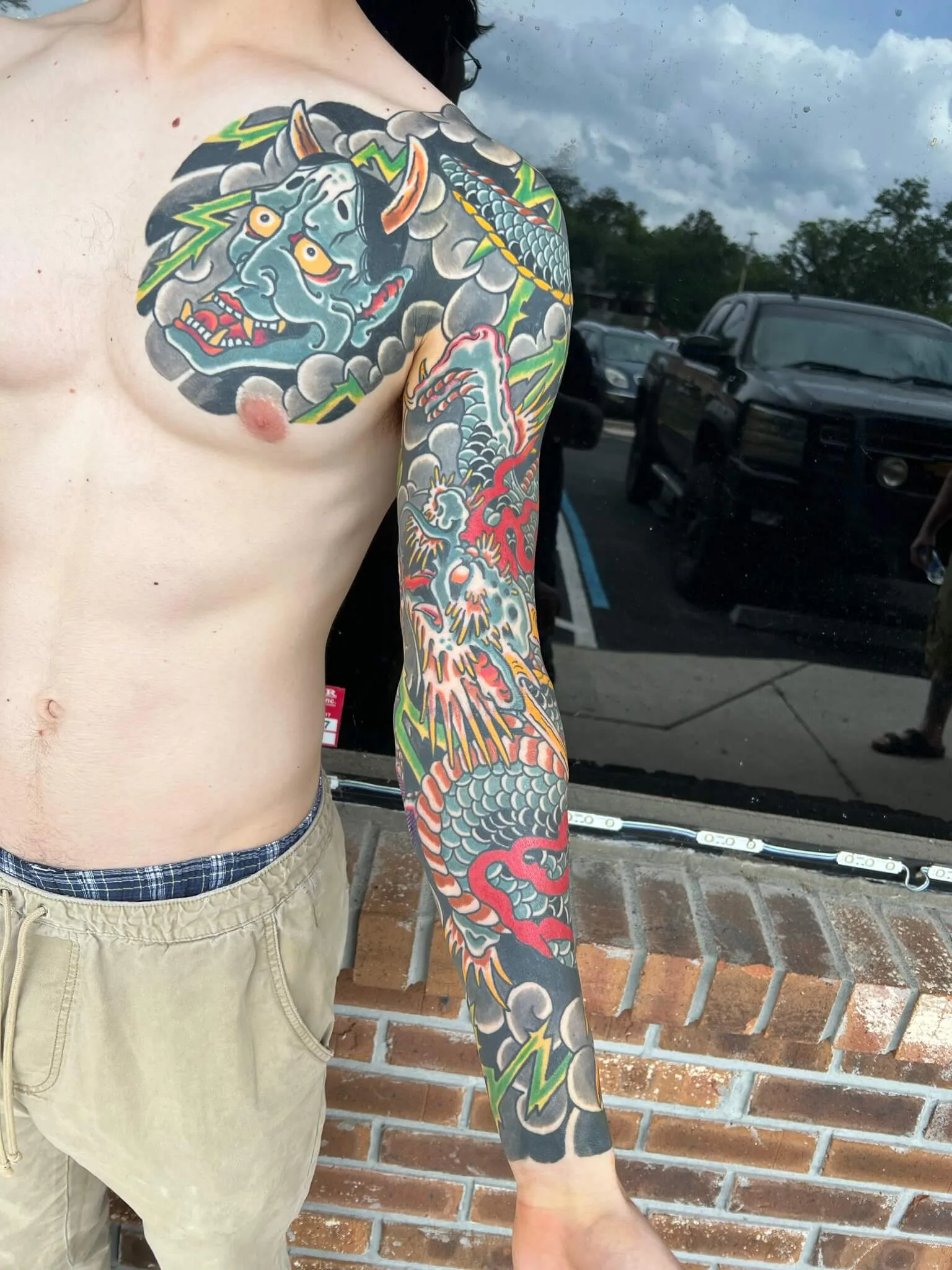 Teal horned demon mask on the shoulder transitioning to a dragon down the arm, with flame details