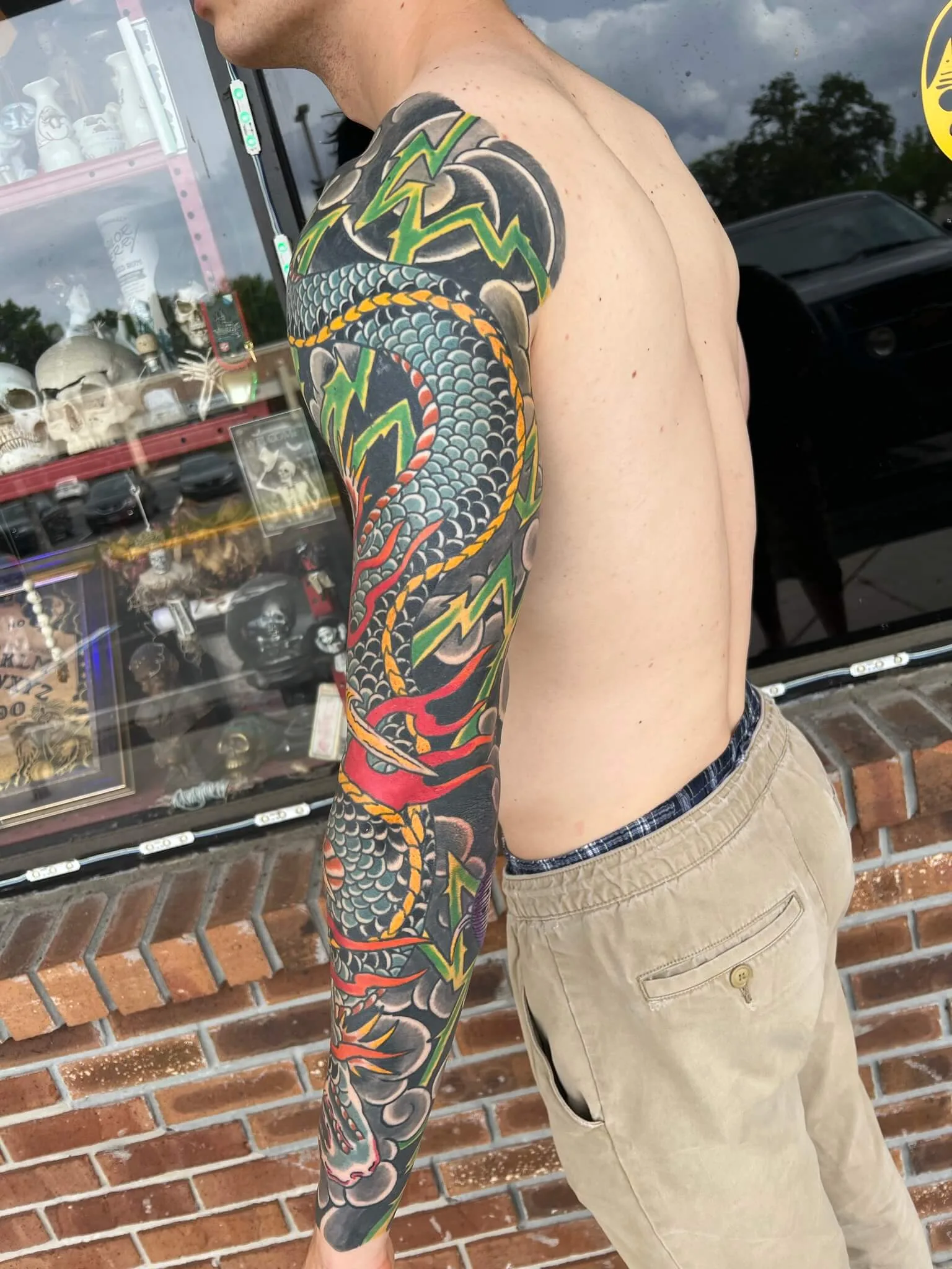 Color full arm sleeve with a blue-grey scaled dragon coiled around green lightning bolts and red flame accents