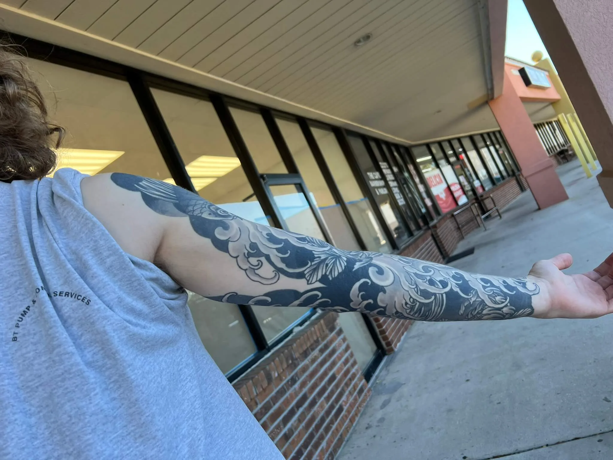Black and grey full arm sleeve with wave and scroll patterns, small fish near the shoulder, to the wrist