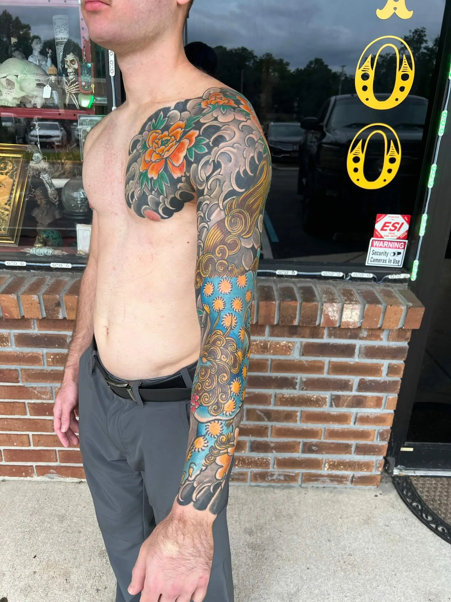 Colour chest and full arm tattoo with an orange peony, grey clouds, and small flowers on a blue background