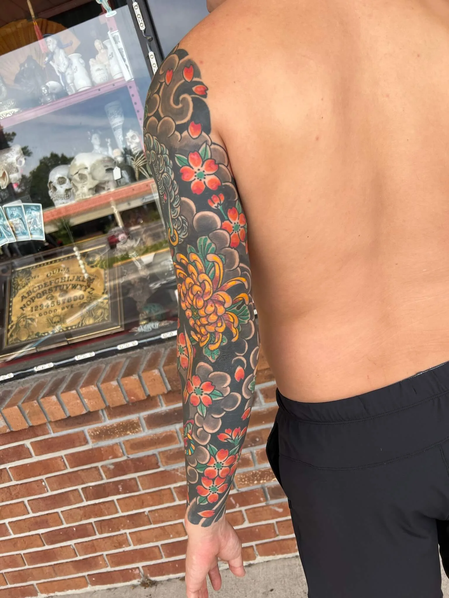 Full arm sleeve of red cherry blossoms and an orange chrysanthemum over grey cloud work on black
